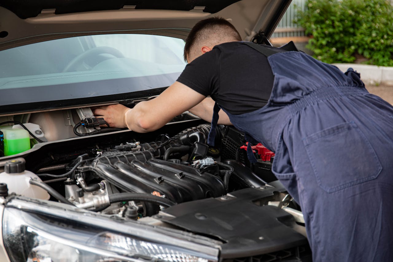 A mechanic performing maintenance work on a cars engine in an outdoor setting.