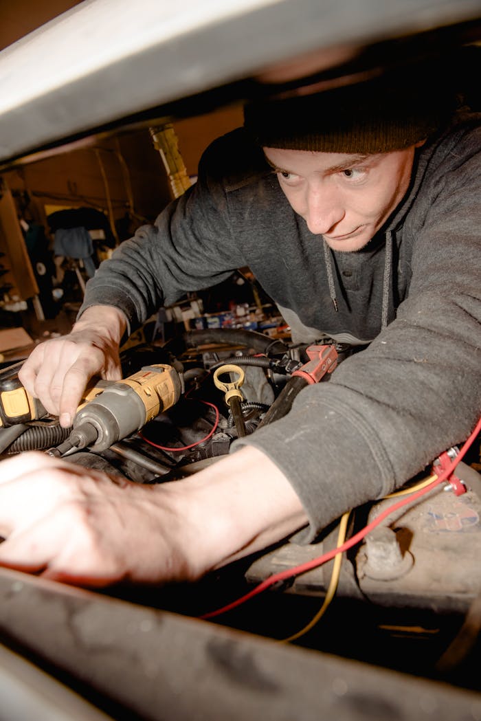 Mechanic intensely focused on repairing a car engine inside a garage using a power tool.
